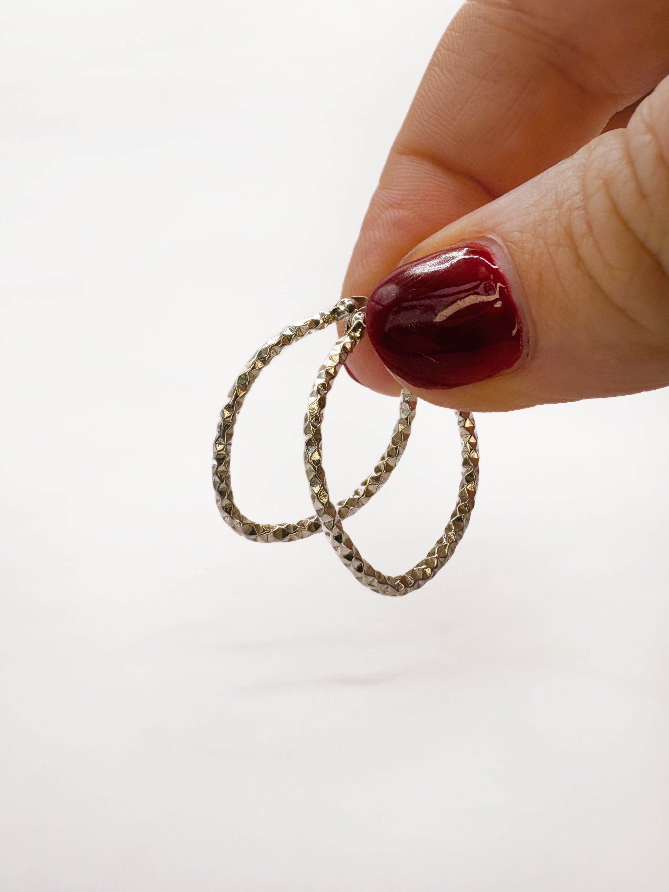 Hand holding two silver diamond cut hoop earrings against a white background
